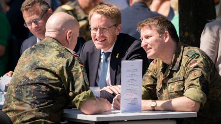 Ministerpräsident Daniel Günther sitzt mit Soldaten in Uniform an einem Tisch und unterhält sich.