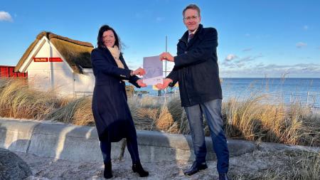 Ministerpräsident Daniel Günther und Bürgermeisterin Bettina Schäfer stehen an einem Strand.