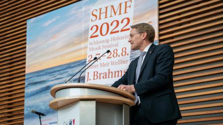 Ministerpräsident Daniel Günther steht an einem Rednerpult. Im Hintergrund hängt ein großes Poster, das auf das SHMF 2022 hinweist. 