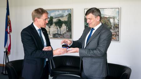 Ministerpräsident Daniel Günther und der slowakische Botschafter stehen sich gegenüber. Daniel Günther übergibt diesem ein Gastgeschenk.