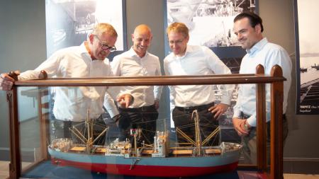 Oliver Berking, Torsten Brocks, Daniel Günther und Philipp Maracke (v.l.) betrachten ein in einer Vitrine ausgestelltes Schiffsmodell