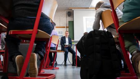 Ministerpräsident Daniel Günther sitzt vor einer Klasse, und liest aus einem Buch vor.
