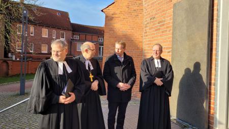 Ministerpräsident Daniel Günther steht vor einer Kirche mit drei Männern in Priestergewändern zusammen.