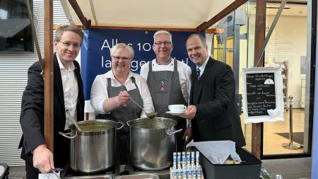 Ministerpräsident Daniel Günther (links) und Landwirtschaftsminister Werner Schwarz (rechts) stehen gemeinsam mit zwei weiteren Personen an einem Stand, der Suppe aus großen Töpfen.