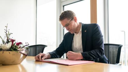 Ministerpräsident Daniel Günther sitzt an einem Tisch und schreibt in einer Mappe.