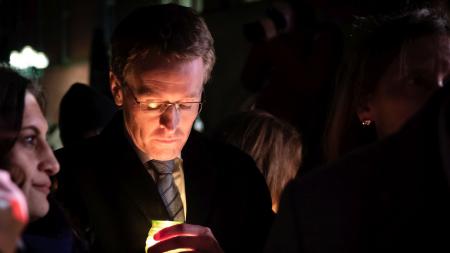 Ministerpräsident Daniel Günther steht in einer Gruppe von Menschen und blickt auf eine Kerze in seinen Händen herab.