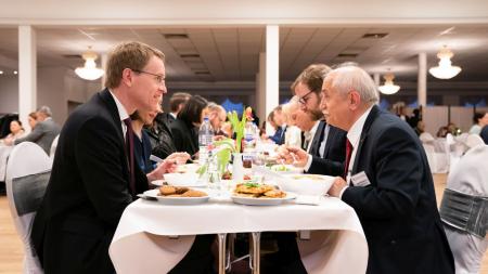 Ministerpräsident Daniel Günther sitzt einem anderen Mann an einem Tisch beim Essen gegenüber. Mit ihnen sitzen weitere Personen am gleichen Tisch.