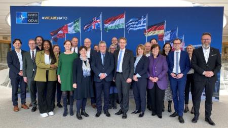 Die gut 20-köpfige Delegation aus Schleswig-Holstein steht gemeinsam mit dem Deutschen Botschafter im Nordatlaktikrat, Rüdiger König, vor einer großen Pressewand. Auf ihr sind die Flaggen der Mitgliedsstaaten abgebildet.