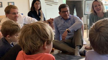 Ministerpräsident Daniel Günther sitzt inmitten von Kindern auf einem Teppich am Boden.