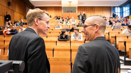 Ministerpräsident Daniel Günther steht neben CAU-Politik-Professor Christian Martin in einem gefüllten Hörsaal.