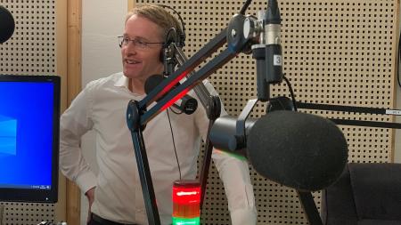 Daniel Günther trägt Kopfhörer und steht in einem Radio-Studio, im Vordergrund sind Mikrofone zu sehen.