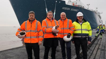 Bundeswirtschaftsminister Habeck, Ministerpräsident Günther, Energiewendeminister Goldschmidt und Frank Schnabel von der Brunsbüttel Ports GmbH stehen vor dem Bug des LNG-Tankers Höegh Gannet.