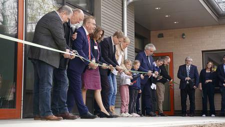 Vor dem neuen Schulgebäude steht Ministerpräsident Daniel Günther und durchtrennt gemeinsam mit zwei Schulkindern und acht weiteren Menschen symbolisch ein Band.