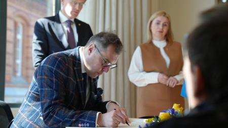 Der ukrainische Botschafter trägt sich in das Gästebuch der Landesregierung ein. Ministerpräsident Daniel Günther und die ukrainische Generalkonsulin schauen ihm dabei über die Schulter.