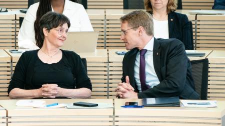 Ministerpräsident Daniel Günther und Finanzministerin Monika Heinold sitzen nebeneinander auf der Regierungsbank im schleswig-holsteinischen Landtag, sie lächeln.