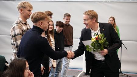 Ministerpräsident Daniel Günther steht in einer Sporthalle und schüttelt mehreren Jugendlichen die Hand. 