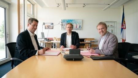 Olaf Schwede, Ministerpräsident Günther und Kai Tellkamp sitzen an einem Tisch und unterzeichnen eine Vereinbarung.