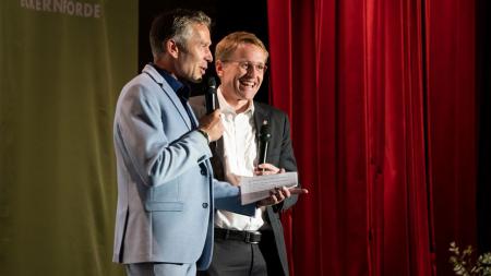 Ministerpräsident Daniel Günther steht lachend neben dem Green-Screen-Festivalleiter Dirk Steffens auf einer Bühne.
