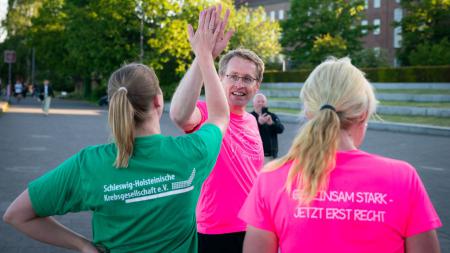 Ministerpräsident Daniel Günther trägt ein Lauftrikot und klatscht mit einer Frau ab, die ein Shirt der schleswig-holsteinischen Krebsgesellschaft trägt. 