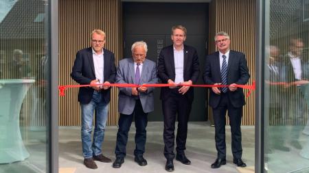 Ministerpräsident Daniel Günther steht mit drei weiteren Personen im Eingang des neuen Verwaltungsgebäudes des Amtes Hüttener Berge. Mit Scheren durchtrennen sie symbolisch ein rotes Band zur Eröffnung.