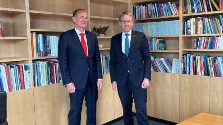 Ministerpräsident Daniel Günther und der niederländische Botschafter Ronald von Roeden stehen nebeneinander vor einem Bücherregal.