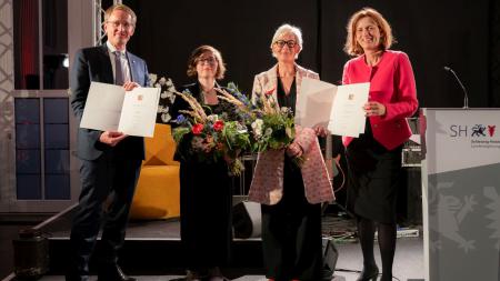 Ministerpräsident Daniel Günther, Nachwuchs-Autorin Zara Zerbe, Kunstpreisträgerin Dörte Hansen und Kulturministerin Karin Prien stehen nebeneinander auf einer Bühne. Die beiden Ausgezeichneten halten Urkunden und Blumensträuße in den Händen.