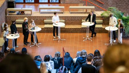 Ministerpräsident Daniel Günther spricht gemeinsam mit acht Schülerinnen und Schülern in einer Aula im Rahmen einer Podiumsdiskussion.