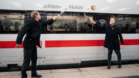 Ministerpräsident Daniel Günther und Berthold Huber aus dem Bahnvorstand taufen einen ICE mit je einem Glas Sekt.