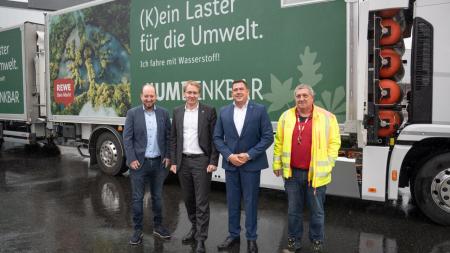 Ministerpräsident Günther steht mit drei anderen Männern vor zwei LKWs, die mit Wasserstoff betankt werden.