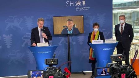 Ministerpräsident Günther, Finanzministerin Heinold und Wirtschaftsminister Buchholz stehen an Rednerpulten. Im Hintergrund steht ein Bildschirm, über den der Northvolt-Geschäftsführer zugeschaltet ist. 