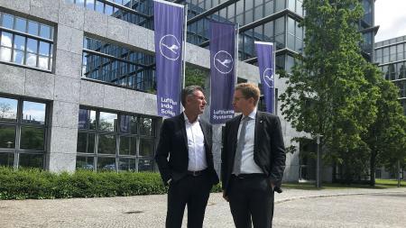 Ministerpräsident Günther (r.) steht mit Bernd Appel vor dem Firmengebäude. Im Hintergrund drei Masten mit Fahnen des Unternehmens.