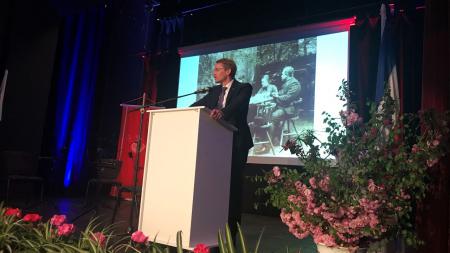 Ein Mann steht an einem Rednerportal. Hinter ihm wird ein schwarz-weißes Foto auf eine Leinwand projiziert.