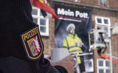 Ein Polizist steht mit einem Becher Kaffee auf einem Schiff, im Hintergrund das WSP Revier Kiel