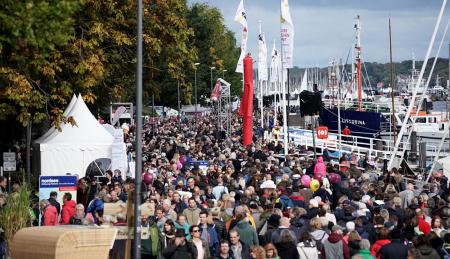 Viele Menschen gehen eine Hafenpromenade entlang.