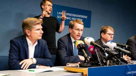 Ministerpräsident Daniel Günther, Gesundheitsminister Garg und Oppositionsführer Ralf Stegner sitzen an einem Tisch. Vor ihnen sind Mikrofone aufgebaut