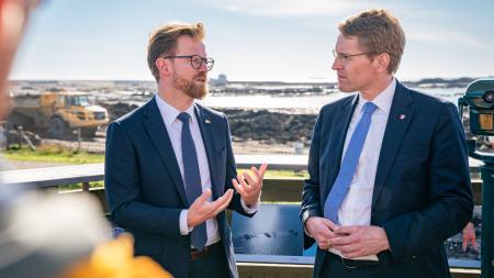 Ministerpräsident Daniel Günther und der dänische Transportminister Benny Engelbrecht im Gespräch vor einer Baustelle.