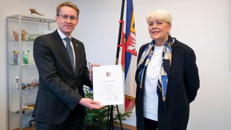 Ministerpräsident Daniel Günther überreicht Uta Fölster in seinem Amtszimmer eine Urkunde.